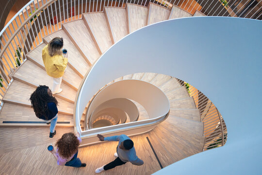 High angle view of colleagues moving up on spiral staircase in office