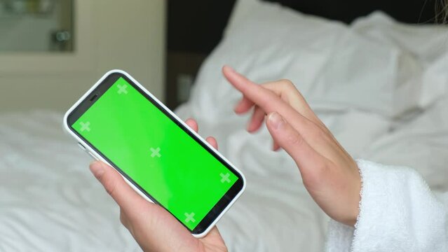 Women's hands in a bathrobe will scroll the phone with a green screen. 4k video. High quality 4k footage