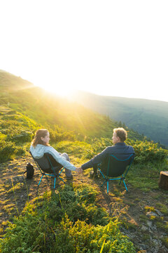 a couple, a man and a woman, sits in a tourist chair on a hill overlooking a mountain range, on the background of mountains, tourism, hiking, time together, family, relationships, nature of the Carpat