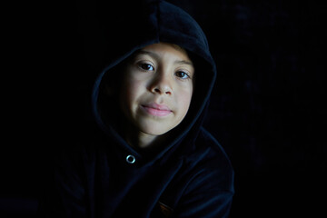 portrait of latin boy's face looking at camera in black hoodie and black background.