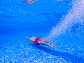 Underwater scene of a young man jumping into the swimming in the pool. Concept of holiday, sport and travel 