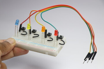 Small breadboard with colorful LED connected using cable and jumper wires to a toggle button held in the hand showing the concept of creation