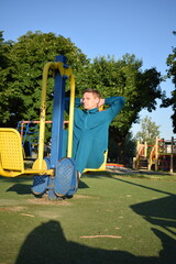 A young man in athletic wear performs morning workout routine at an outdoor gym. He trains...
