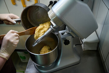Qualified woman baker adding pastry dough into big kitchen mixer