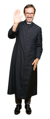 Middle age priest man wearing catholic robe Waiving saying hello happy and smiling, friendly...