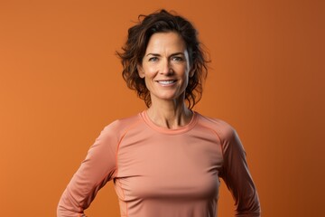 Obraz premium Portrait of a tender woman in her 40s wearing a moisture-wicking running shirt isolated on pastel orange background
