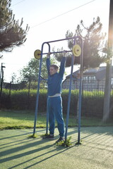 A young man in athletic wear performs morning workout routine at an outdoor gym. He trains...