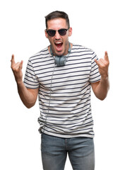 Naklejka premium Handsome young man wearing headphones shouting with crazy expression doing rock symbol with hands up. Music star. Heavy concept.