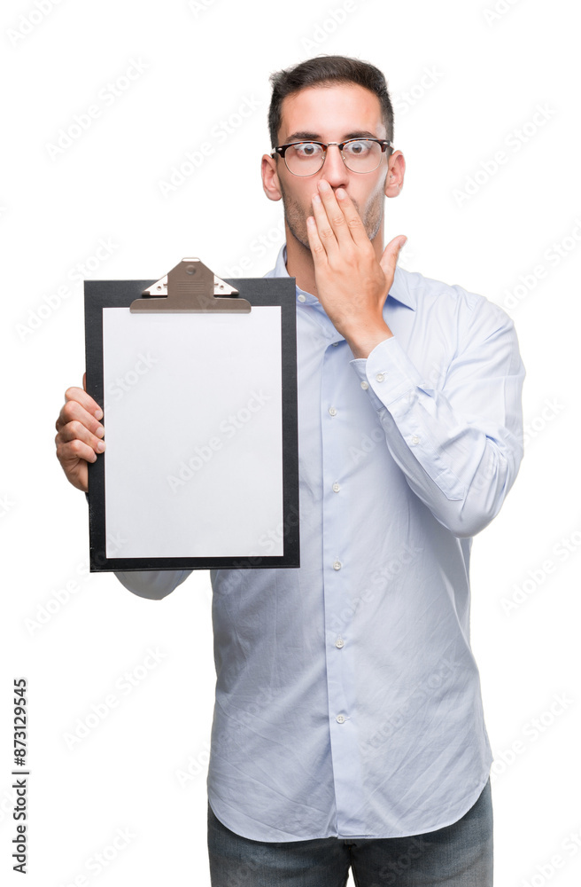 Wall mural Handsome young business man showing a clipboard cover mouth with hand shocked with shame for mistake, expression of fear, scared in silence, secret concept