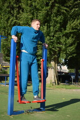 A young man in athletic wear performs morning workout routine at an outdoor gym. He trains...