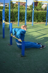 A young man in athletic wear performs morning workout routine at an outdoor gym. He trains...