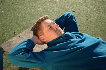 A young man in athletic wear performs morning workout routine at an outdoor gym. He trains...