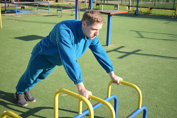 A young man in athletic wear performs morning workout routine at an outdoor gym. He trains...