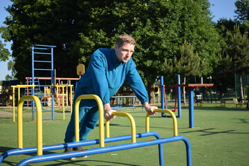 A young man in athletic wear performs morning workout routine at an outdoor gym. He trains...
