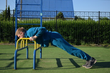 A young man in athletic wear performs morning workout routine at an outdoor gym. He trains...