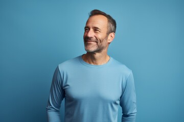 Fototapeta premium Portrait of a satisfied man in his 40s showing off a lightweight base layer on soft blue background