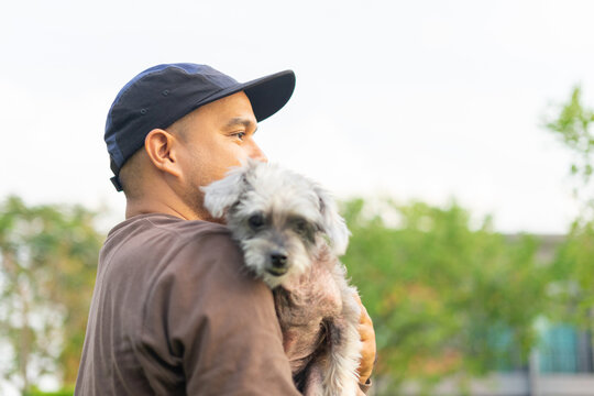 Yong asian man in casual outfit of cheerful with old dog at outdoors. Male playing with her little adopted dog pet and owner having good time together. Hugs and kisses, Love, Care, Friendship
