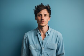 Portrait of a tender man in his 20s sporting a versatile denim shirt isolated on soft blue background
