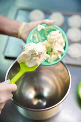 Professional woman confectioner adding white creamy mixture into mixer bowl