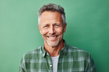 Fototapeta premium Portrait of a smiling man in his 50s wearing a comfy flannel shirt on soft green background