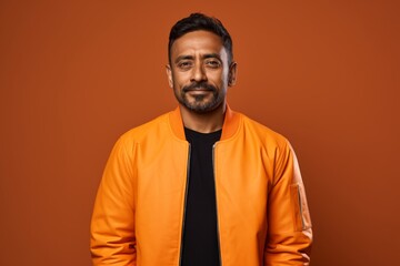 Obraz premium Portrait of a content indian man in his 40s wearing a trendy bomber jacket isolated on soft orange background