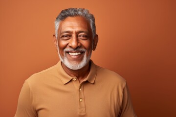Obraz premium Portrait of a cheerful indian man in his 60s sporting a breathable mesh jersey while standing against soft brown background