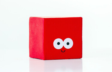 Red toy block smiling with eyes on white background representing happiness and fun