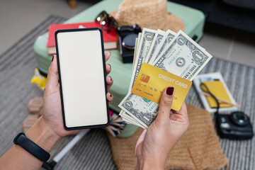 A woman's hand holding a smartphone with a white screen, along with clothes being packed into a suitcase in preparation for a weekend trip