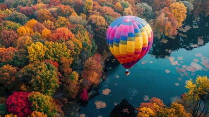 Fototapeta premium A vibrant hot air balloon soars over a tranquil lake, surrounded by a stunning autumn forest with varied foliage colors.