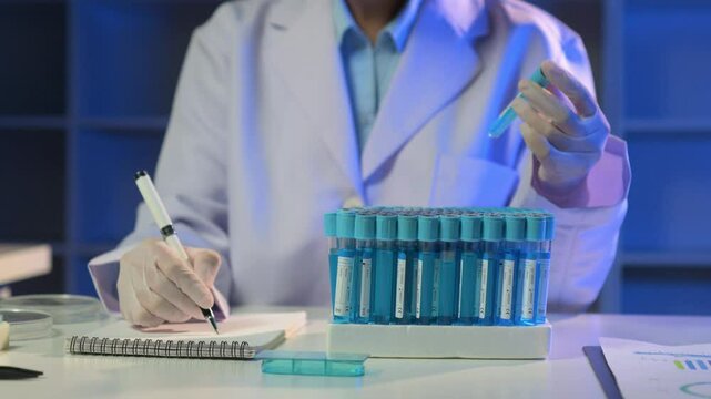 Scientist in lab coat analyzing blue test tubes and meticulously recording data in a laboratory. Documentation process with scientific precision