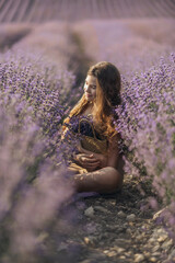 Girl is sitting in a field of purple flowers. She is holding a basket of flowers and smiling. Scene is peaceful and serene, as the girl is surrounded by the beauty of nature.