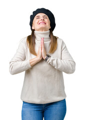 Middle age mature woman wearing winter sweater and beret over isolated background begging and...