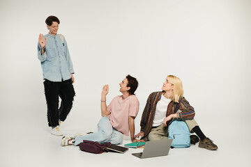 Fototapeta premium Three young students, dressed in casual attire, stand and sit on a white background, displaying camaraderie and connection.