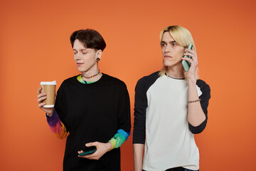 Two young queer friends pose in vibrant attire against an orange backdrop.