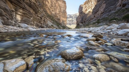 A clear river flowing over smooth stones in a deep canyon, with steep rock walls rising on either side.