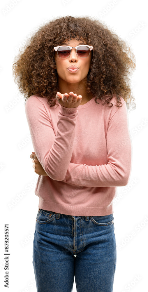 Wall mural african american woman wearing pink sunglasses looking at the camera blowing a kiss with hand on air