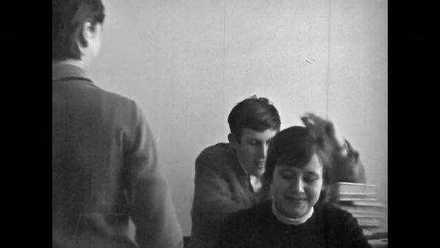 Adult students sitting at school desks, teacher conducting lesson in university classroom. School, university learning atmosphere. Vintage black white film. Education college archive. Retro 1980s