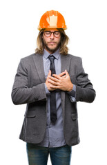 Young handsome architec man with long hair wearing safety helmet over isolated background smiling with hands on chest with closed eyes and grateful gesture on face. Health concept.