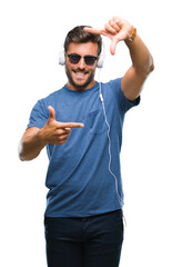 Fototapeta premium Young handsome man wearing headphones listening to music over isolated background smiling making frame with hands and fingers with happy face. Creativity and photography concept.