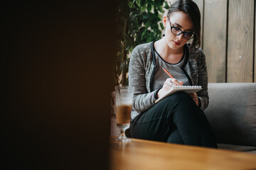Young businesswoman working in a cafe, writing notes and brainstorming ideas while enjoying a...