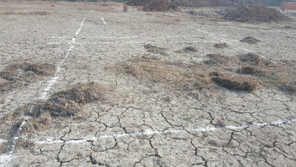  The image shows a dry, cracked field with a white boundary line marked on it. There is a pile of...