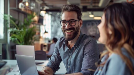 Smiling businessman collaborating with female colleague on laptop in open office space