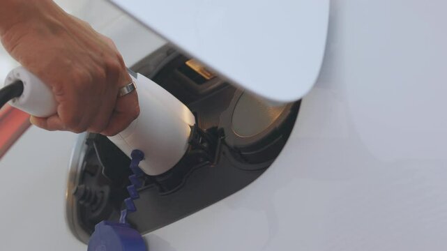Close-up of hand plugging off charger from electric vehicle (EV), and ready to go. It shows sustainability, green technology, renewable energy, environmental conservation, and zero-emission vehicles. 