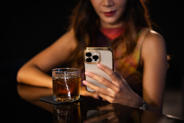 Woman sitting at bar using phone with her glass of alcohol.