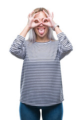 Young blonde woman over isolated background doing ok gesture like binoculars sticking tongue out, eyes looking through fingers. Crazy expression.