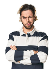 Young Caucasian man in studio setting frowning face in displeasure, keeps arms folded.