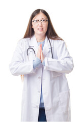 Young Chinese doctor woman over isolated background begging and praying with hands together with hope expression on face very emotional and worried. Asking for forgiveness. Religion concept.