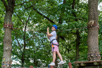 Beautiful woman in helmet doing rope course on tree in forest with peace sign and wide smile on sunny day. Concept of active lifestyle, sports entertainment and sports equipment. High quality photo 