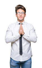 Young business man wearing glasses over isolated background praying with hands together asking for forgiveness smiling confident.