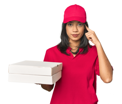 Latina delivering pizza, studio setup pointing temple with finger, thinking, focused on a task.